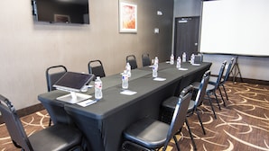 A conference room with a long table, chairs, water bottles, a projector screen, and a TV on the wall. - Chic hotel with AC and fitness room in marvelous Houston (Houston)