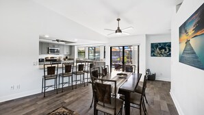 A modern kitchen with a central island, a dining area with a long table and chairs, and a large window providing a view of the outdoors. - SEASIDE VILLA MANATEE BAY in quiet location on Pine Island (Saint James City)