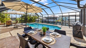 An outdoor patio with a pool, dining table set with plates and glasses, and umbrellas. - SEASIDE VILLA MANATEE BAY in quiet location on Pine Island (Saint James City)