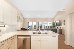 Enjoy cooking in this well-lit kitchen with a central island, white cabinetry, and a large window offering a view of the outdoor seating area.
