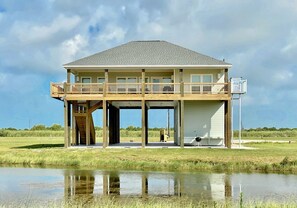 Situated beside a serene body of water, this two-story building offers a balcony on the upper level, supported by visible beams and columns.