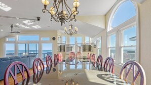 Un vaste espace dédié à la salle à manger, avec une table en verre, des chaises rouges et violettes, et un lustre.