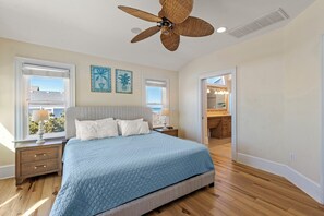 A bedroom with a large bed, a ceiling fan, and two windows with blinds. - The Sun: Oceanfront | Pool | Hot Tub | Elevator (Nags Head)