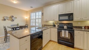 Une cuisine avec des meubles blancs, un plan de travail en granit, un lave-vaisselle, une cuisinière et un four à micro-ondes.
