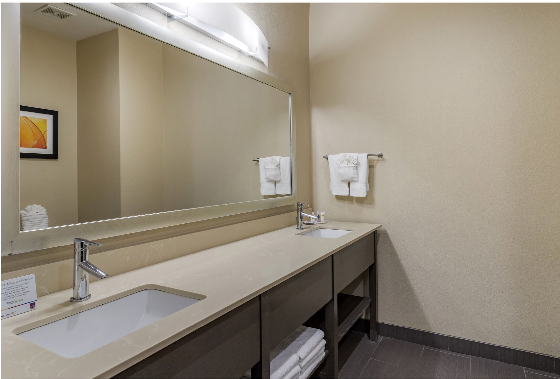 A hotel bathroom with a large mirror, two sinks, and a towel rack.