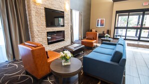 A lobby with a fireplace, leather sofas, a blue couch, and a round table with a vase of flowers. - Comfort Suites Near Sam Houston Race Park (Houston)
