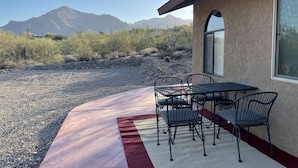 Une terrasse avec une table et des chaises, un tapis rouge et blanc, et une vue sur les montagnes en arrière-plan.