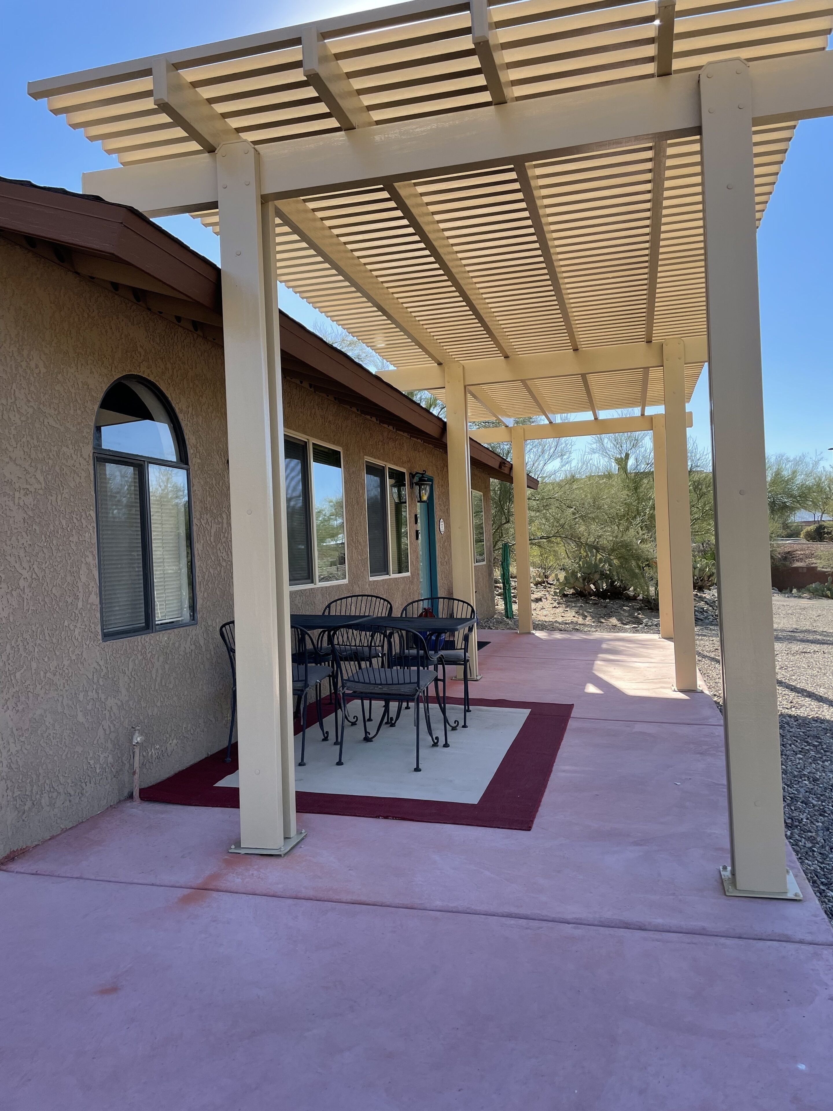 A covered patio area with a table and chairs, a red carpet, and a building with arched windows.