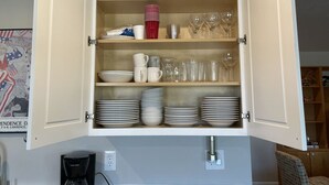 Un meuble de cuisine doté d’étagères où sont empilées des assiettes, des bols, des tasses et des verres à vin.