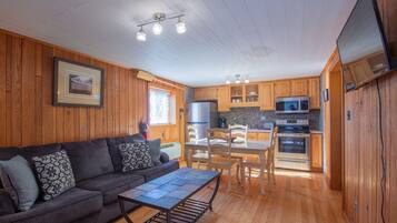 A cozy cabin interior with a wooden interior, a sofa, a dining table, and a kitchen area with appliances.