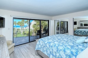 A bedroom with a large bed, a TV, and a balcony with a view of palm trees and the ocean. - Doveplum 220-2 level 2BR/2.5BA townhome has tropical views overlooking both pool and Gulf (Sarasota)