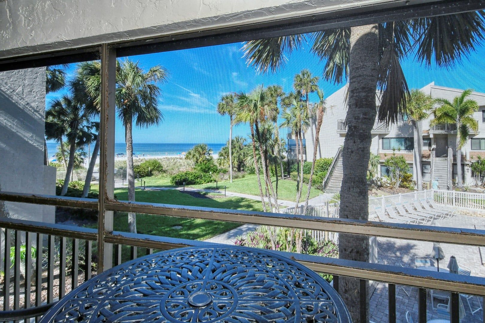 A balcony with a view of a beach, palm trees, and a building with a staircase.