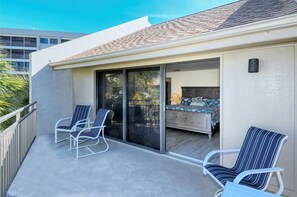 A balcony with two chairs and a bed with a blue bedspread.