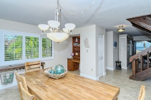 A dining area with a wooden table, a chandelier, and a view through a window with blinds. - Doveplum 220-2 level 2BR/2.5BA townhome has tropical views overlooking both pool and Gulf (Sarasota)