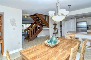 A spacious kitchen with a wooden staircase, a dining area with a wooden table and chairs, and a chandelier.