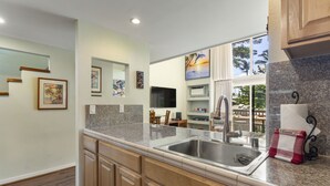 Una cocina con encimeras de granito, pileta de acero inoxidable, armarios de madera y lavavajillas.
