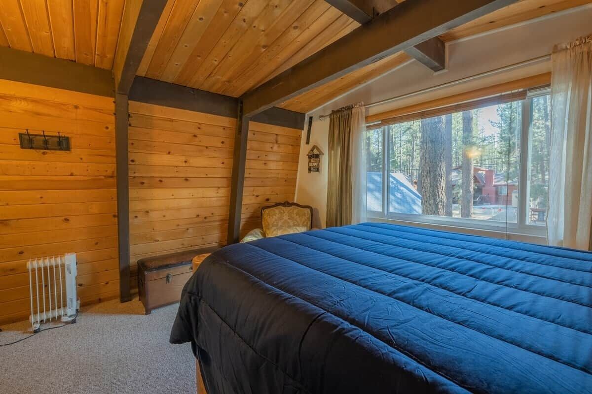 Una habitación de cabaña de madera con una cama, un radiador, una ventana con cortinas y una silla.