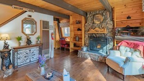 A cozy cabin interior with a fireplace, wooden walls, a sofa, and a welcome sign.