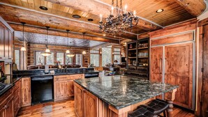 Uma cozinha ampla com armários de madeira, uma ilha grande com banquetas e um lustre.