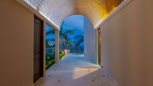 A corridor with a tiled floor leading to a balcony with a view of a hillside and palm trees. - Villa Del Mar-5 Star Luxury Villa with Epic Views (Cabo San Lucas)