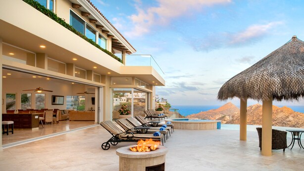 A modern outdoor lounge area with a fire pit, lounge chairs, and a thatched umbrella. - Villa Del Mar-5 Star Luxury Villa with Epic Views (Cabo San Lucas)