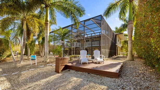 A modern building with a glass facade, surrounded by palm trees and a deck with chairs.