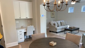 A modern living room with a round wooden table, a sofa, and a coffee table. There is a kitchen area with white cabinets and a dining table with chairs. - Family Home Near LakePoint Sports with Fenced Yard (Acworth)