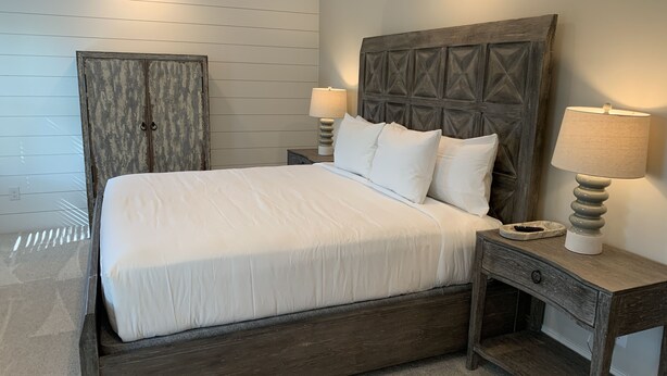 A neatly made bed with white bedding, a wooden headboard, two bedside lamps, and a small bedside table with a lamp. - Family Home Near LakePoint Sports with Fenced Yard (Acworth)