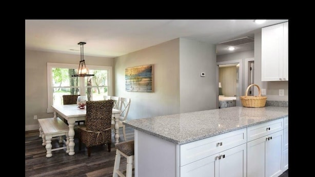 A kitchen with white cabinets, a granite countertop, and a dining area with wicker chairs and a white table. - Discover Anchors Down, a charming 3-bedroom duplex in Oak Island, perfect for family getaways! (Oak Island)