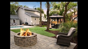 A backyard with a stone fire pit, a pool, and outdoor furniture. - Discover Anchors Down, a charming 3-bedroom duplex in Oak Island, perfect for family getaways! (Oak Island)