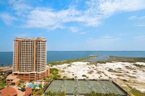 A high-rise hotel with multiple floors, a tennis court, and a beach view.