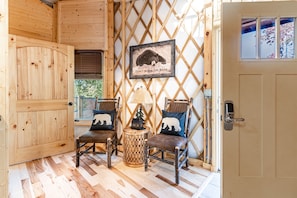 Un intérieur en bois avec une porte, deux chaises dotées de coussins à motifs d’ours, une lampe et un cadre photo fixé au mur, contenant une illustration d’un ours.