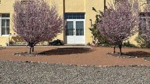 A building with a yellow facade, a central arched entrance, and two flowering trees in front. - Historic Schoolhouse Flat by Verde Canyon Railroad (Clarkdale)