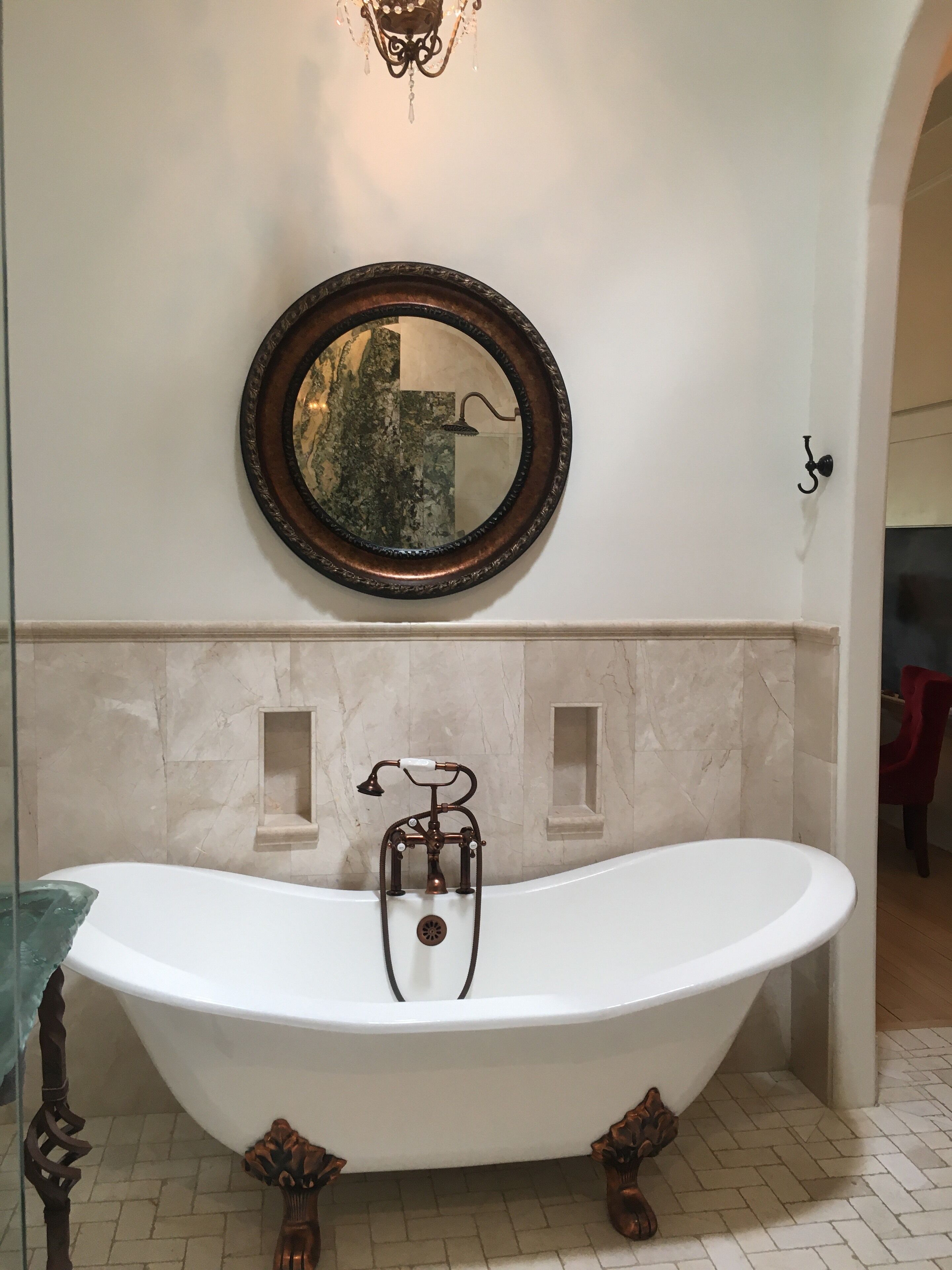 Una bañera independiente con diseño vintage, un espejo instalado en la pared y una lámpara sobre el espejo.