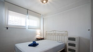 Een slaapkamer met een bed, nachtkastje, lamp en een dressoir.