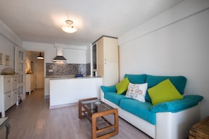 A compact living space with a kitchenette, a sofa with colorful cushions, and a glass coffee table.