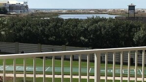 A balcony with a view of a beach, a tennis court, and a building with a tower. - Fun & Easy Access to Everything! Islander 216 (Destin)
