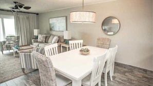 A modern living room with a white dining table, wicker chairs, a ceiling fan, and a large mirror on the wall. - Fun & Easy Access to Everything! Islander 216 (Destin)
