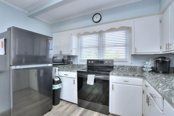 A modern kitchen with stainless steel appliances, white cabinetry, and a clock on the wall. - Experience coastal charm at Dolphin Delight, a 3BR, 2BA home in Oak Island with ocean views. (Oak Island)