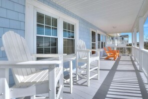 A covered porch with white Adirondack chairs and a table, blue siding, and a view of the ocean. - Experience coastal charm at Dolphin Delight, a 3BR, 2BA home in Oak Island with ocean views. (Oak Island)