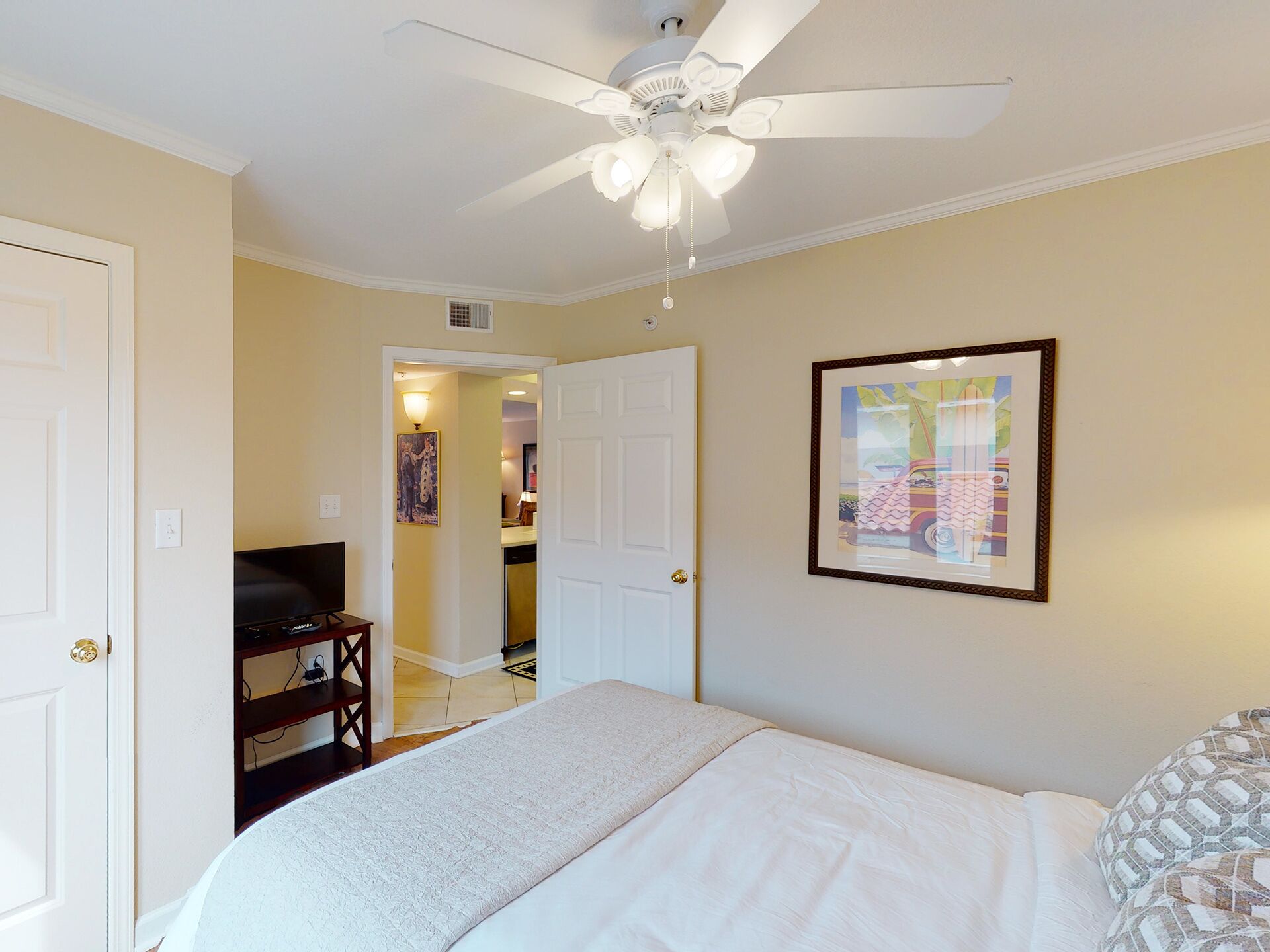 A bedroom with a bed, a ceiling fan, a door, and a framed picture on the wall.