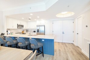 A modern kitchen with white cabinets, a blue island, and a stainless steel refrigerator.