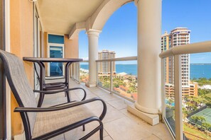A balcony with two chairs, a view of the sea, and high-rise buildings in the background.