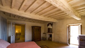 A bedroom with a bed, a wooden wardrobe, a chair, a small table, and a door leading to another room. - View on the Vally (Cetona)