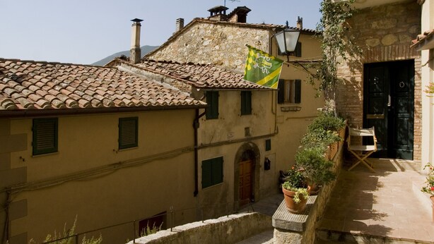 A narrow cobblestone street with traditional stone buildings, a flag, and a staircase leading to an entrance. - View on the Vally (Cetona)