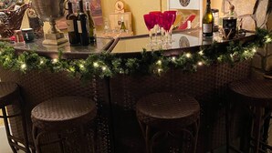 Een bar met rieten krukken, een bar een barblad versierd met groen en een fles wijn.