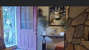 Een knus ingerichte kamer met een houten vloer, een rieten stoel, een klein tafeltje met een rode tafelkleed en een stenen muur.