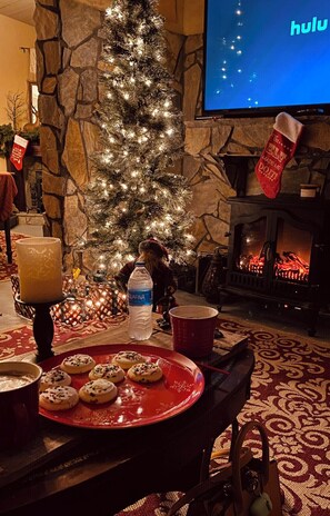 Una sala de estar acogedora con chimenea de piedra, un árbol de Navidad iluminado y un televisor de pantalla plana mostrando el logotipo de Hulu.