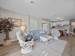 A modern living room with a sofa, chair, and coffee table, a kitchen with white cabinets, and a dining area with a table and chairs. - Spacious 3rd-Row Beach Home with Private Saltwater Pool (Emerald Isle)