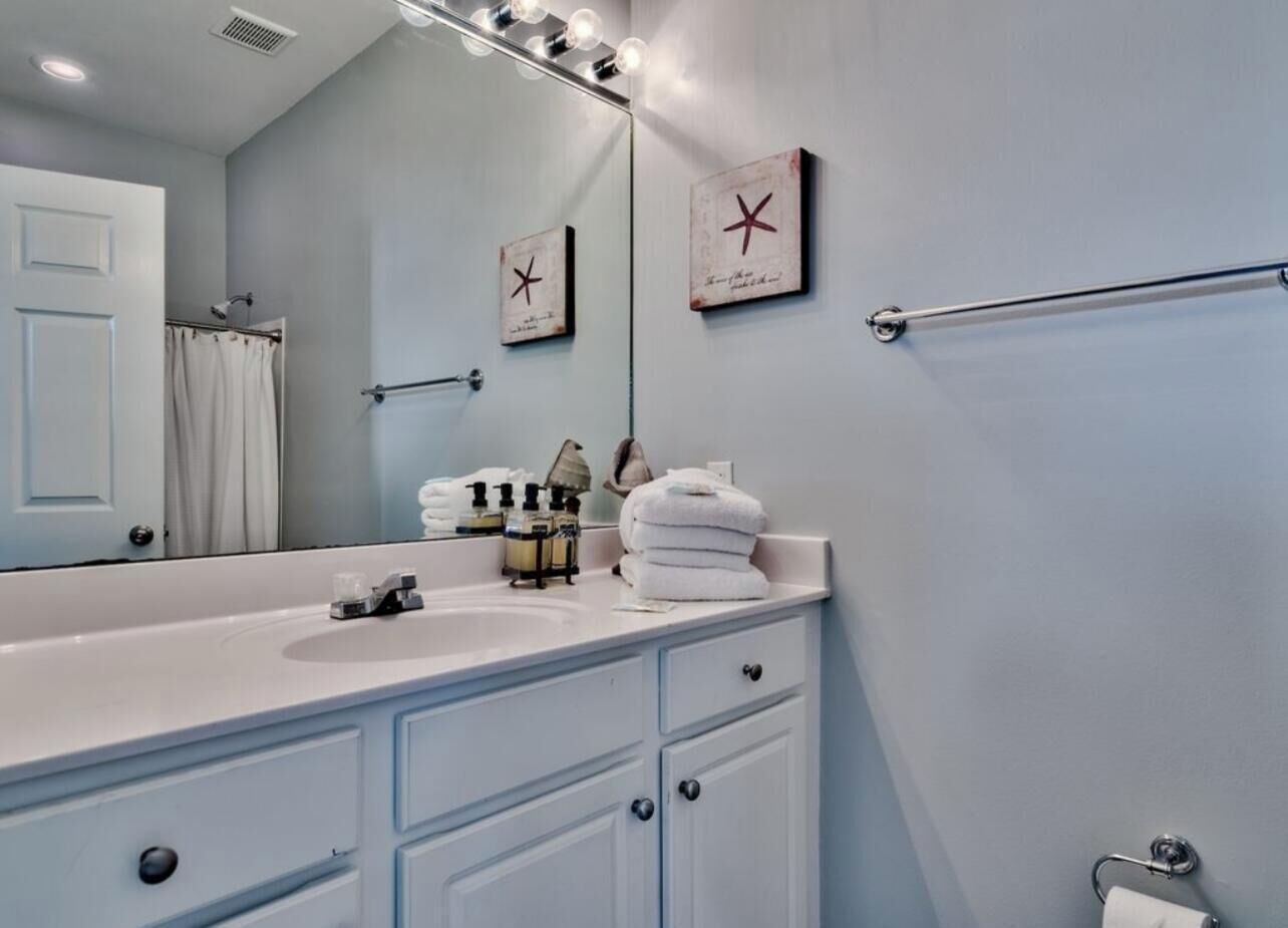 A bathroom with a white vanity, a mirror, a towel rack, and a towel dispenser.